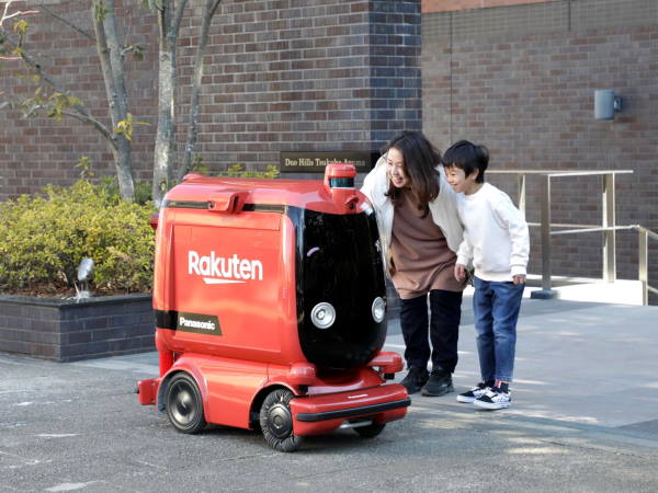 楽天グループ、パナソニック ホールディングスおよび西友の3社は、国内初の自動配送ロボット（UGV）の公道走行によるスーパーからの商品配送サービスを実現した 配送先にUGVが到着し、商品を受け取るユーザー